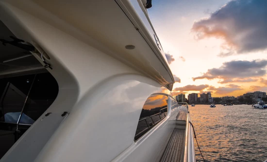 Close-up of Allegra's hull and side deck at sunset, city skyline reflected in the window