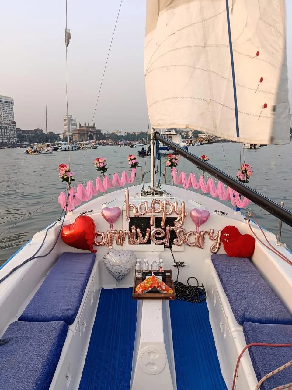 A 'Happy Anniversary' balloon display at the bow with rose bouquets, the Gateway of India visible across the water