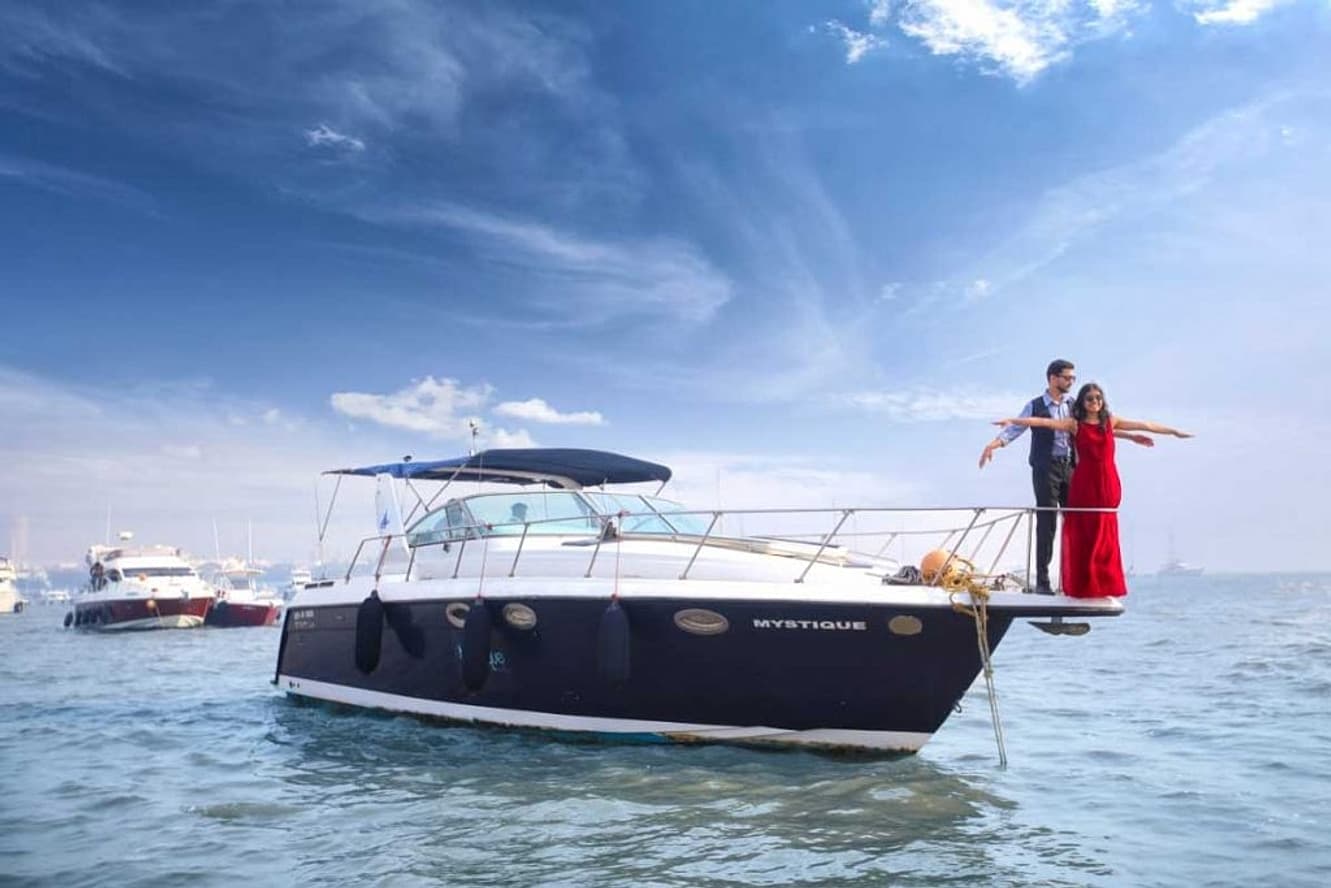 A couple at the bow of a motor yacht off Mumbai, arms outstretched, moments before a proposal