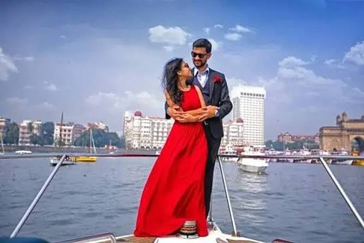 A couple in a red dress and suit on a motor yacht bow with the Gateway of India and Taj Mahal Palace Hotel behind